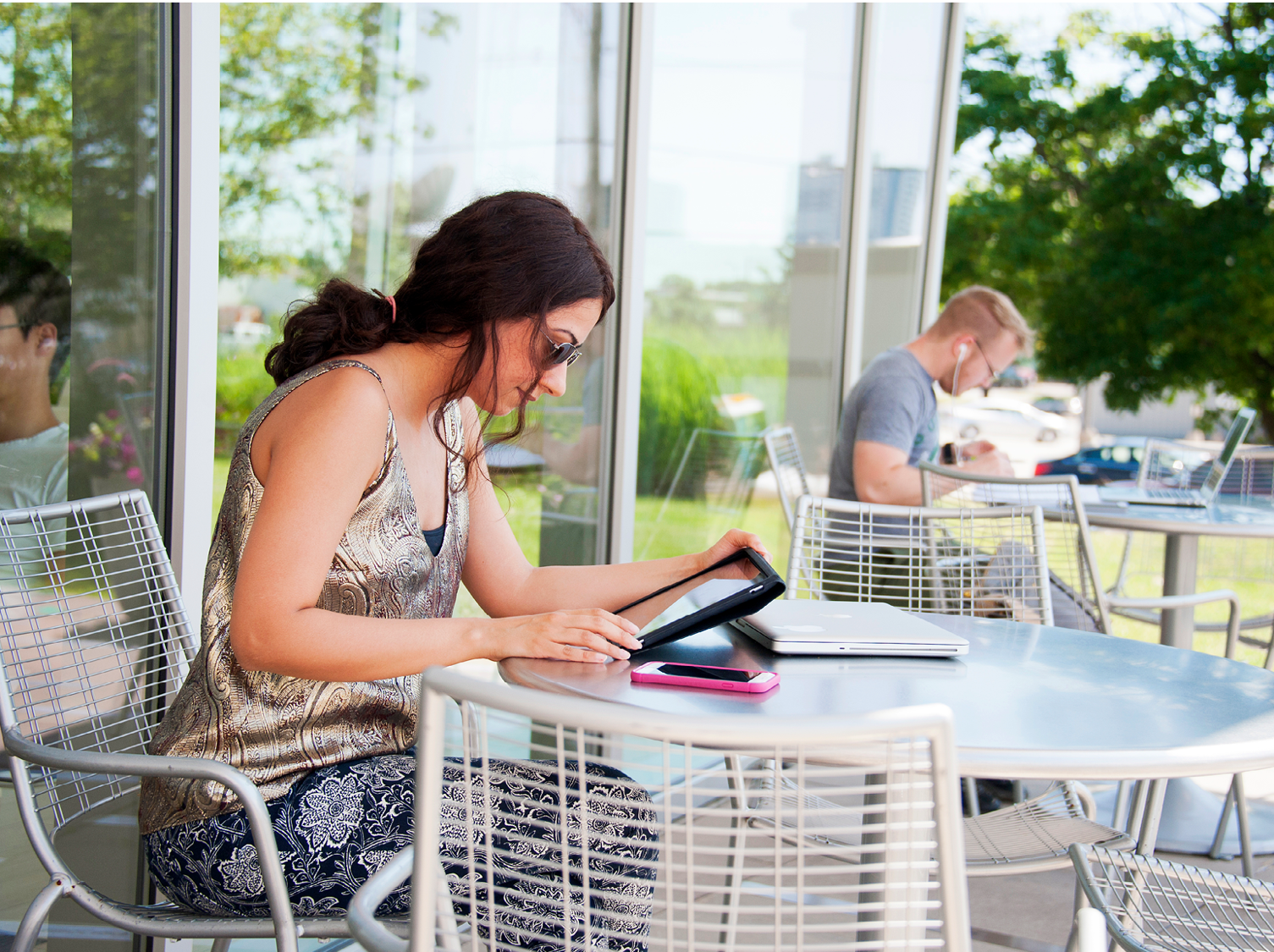 woman seated at patio table using tablet, at the library