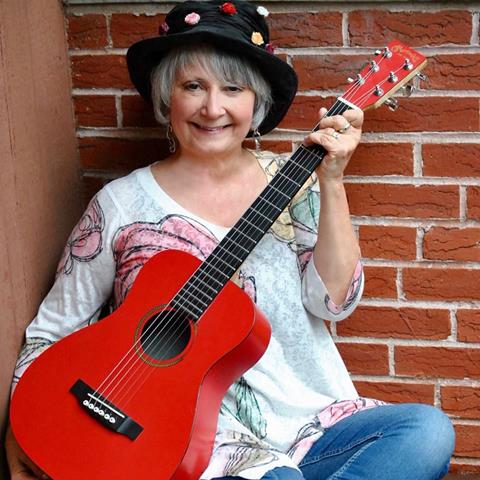 portrait of Jodi Kopplin holding red guitar, wearing black hat with buttons